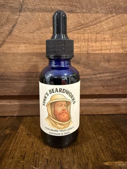 The Beekeeper "Premium Beard Oil - Honey & Bourbon Blend 1oz" in a blue bottle on a wooden background.