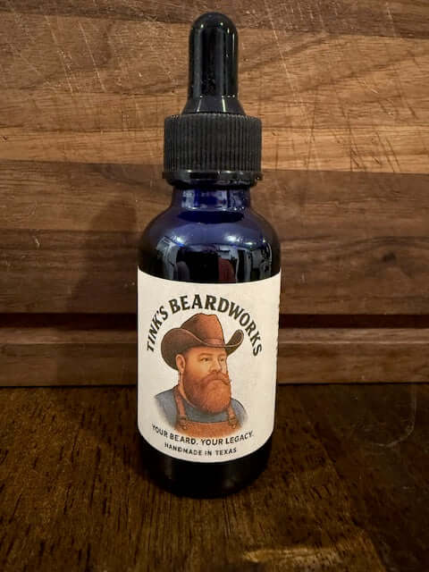 The Cowboy "Premium Beard Oil - Leather & Sweet Tobacco Blend 1oz" in a blue bottle with Tink's Beardworks label.